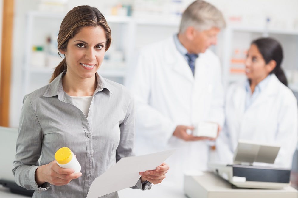 Woman smiling while holding a bottle of pills and a prescription